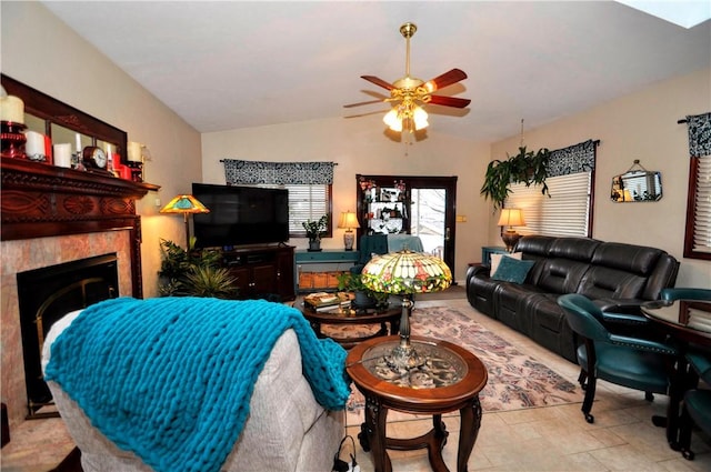 living area featuring vaulted ceiling, a ceiling fan, and a tile fireplace