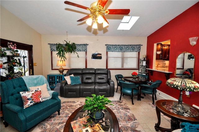 living area featuring lofted ceiling with skylight, a ceiling fan, and baseboards