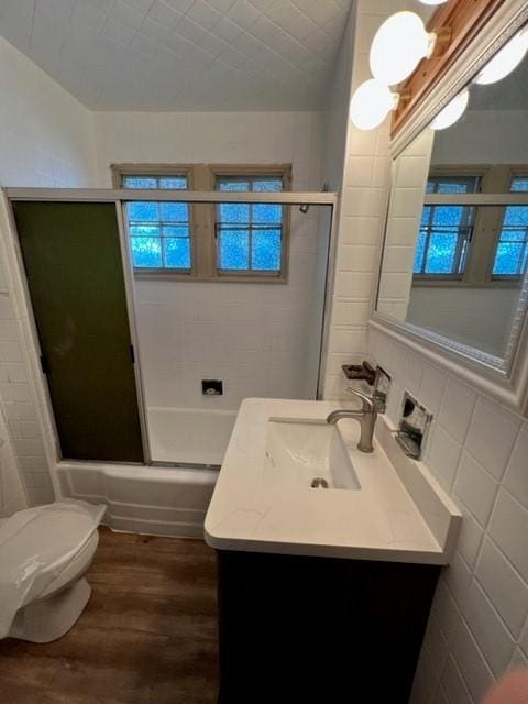 full bath featuring toilet, wood finished floors, combined bath / shower with glass door, tile walls, and vanity