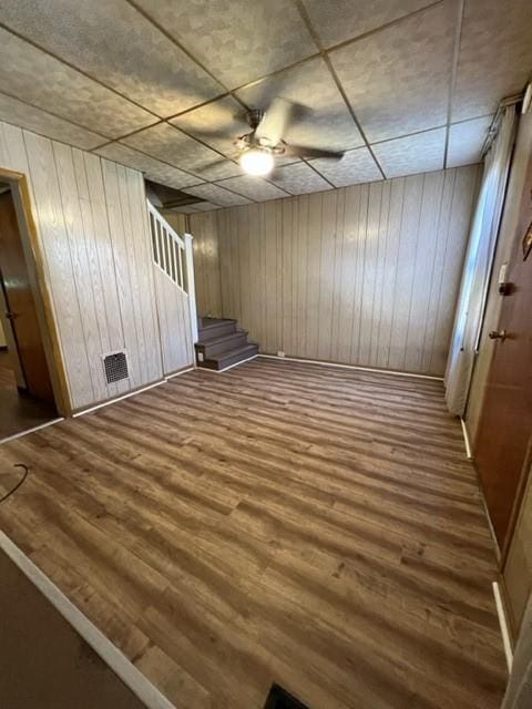 unfurnished room with stairway, a ceiling fan, wood finished floors, visible vents, and wood walls