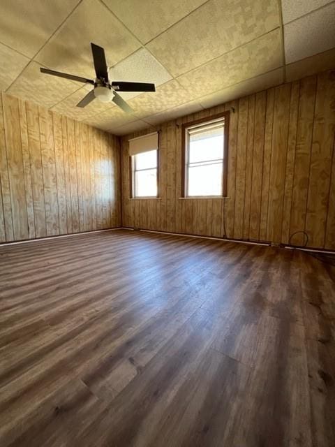 unfurnished room featuring dark wood-type flooring, wooden walls, and a ceiling fan