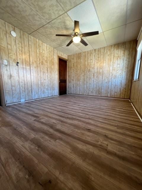 unfurnished room featuring wooden walls, ceiling fan, and wood finished floors