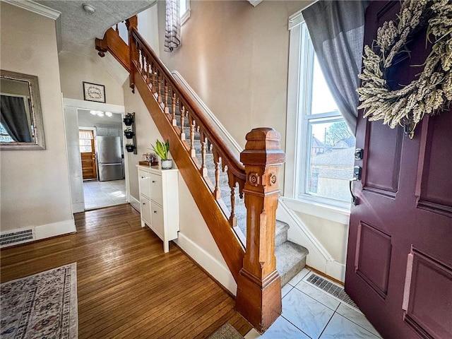 foyer entrance featuring visible vents, wood finished floors, baseboards, a towering ceiling, and stairs