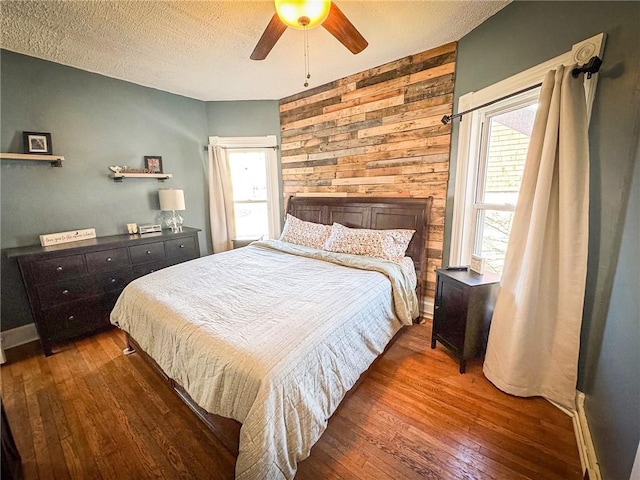 bedroom featuring baseboards, ceiling fan, hardwood / wood-style flooring, wood walls, and a textured ceiling