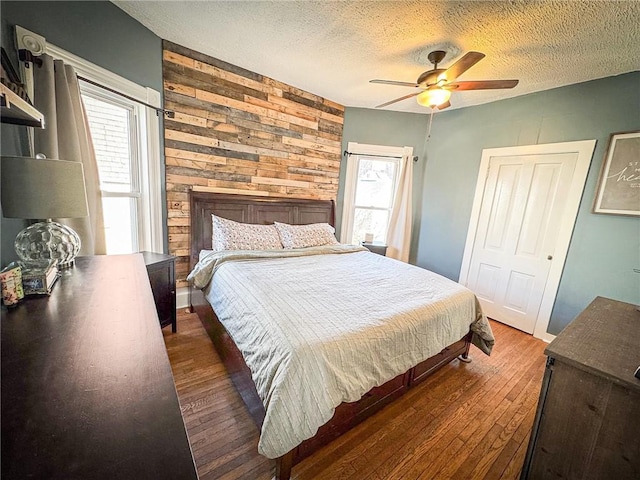 bedroom featuring wooden walls, a ceiling fan, wood-type flooring, and a textured ceiling