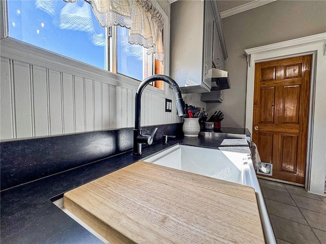 kitchen featuring dark countertops, a sink, crown molding, and dark tile patterned flooring