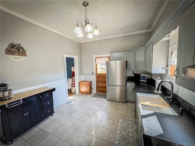 kitchen with a sink, appliances with stainless steel finishes, wainscoting, crown molding, and light tile patterned floors