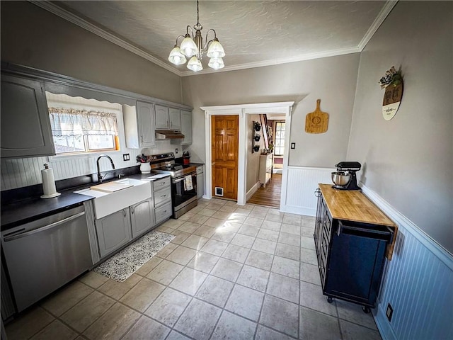 kitchen featuring a sink, stainless steel appliances, under cabinet range hood, wainscoting, and crown molding