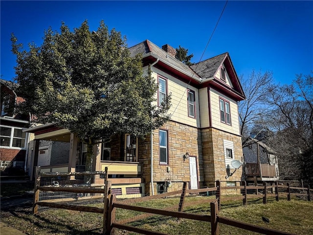 view of side of property featuring a fenced front yard, a porch, roof with shingles, a chimney, and stone siding