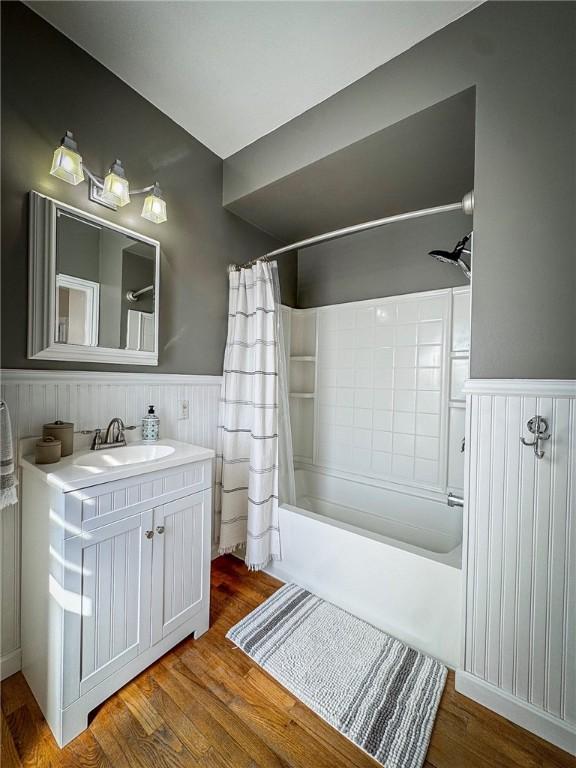 full bath with vanity, shower / tub combo, wood finished floors, and wainscoting