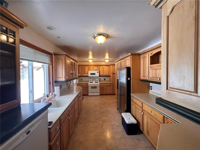 kitchen with a sink, white appliances, brown cabinetry, light countertops, and glass insert cabinets