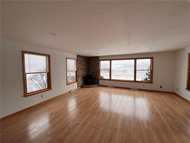 unfurnished living room featuring visible vents, baseboards, light wood-style floors, and a brick fireplace