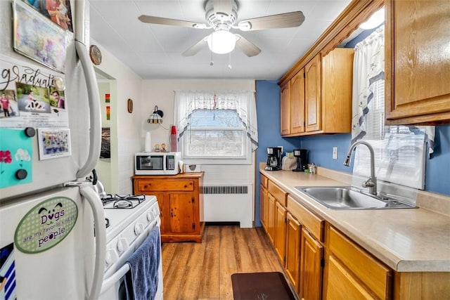 kitchen with white appliances, radiator, brown cabinetry, a sink, and light countertops