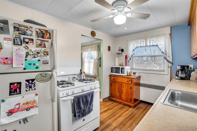 kitchen featuring light wood finished floors, a sink, white appliances, radiator, and light countertops