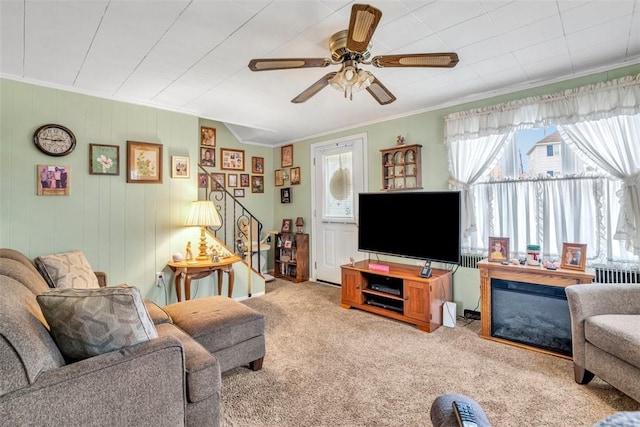 carpeted living room with stairs, crown molding, and ceiling fan