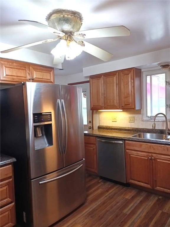 kitchen with dark countertops, a sink, brown cabinets, appliances with stainless steel finishes, and dark wood-style flooring