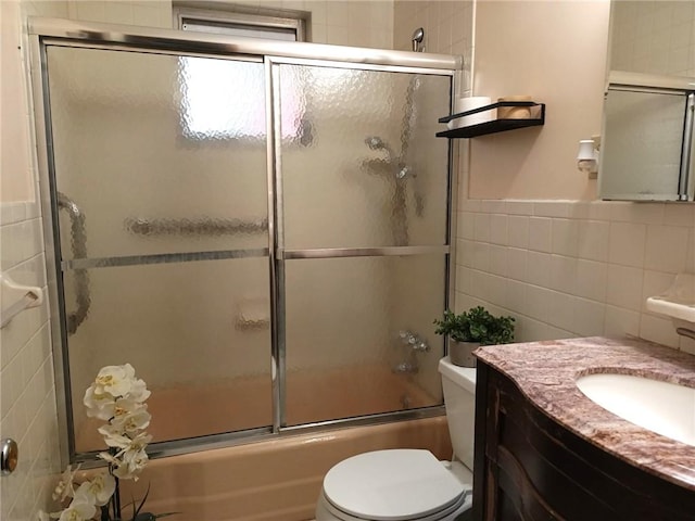 full bath featuring toilet, tile walls, vanity, and shower / bath combination with glass door