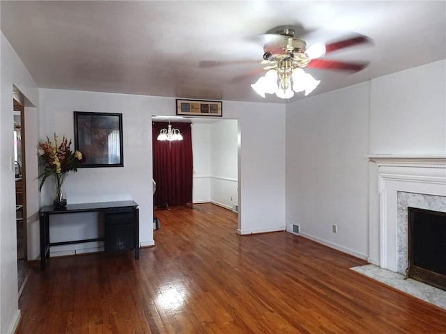 unfurnished living room featuring ceiling fan with notable chandelier, a fireplace, baseboards, and hardwood / wood-style flooring