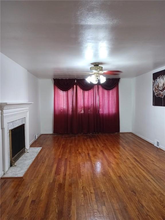 unfurnished living room with ceiling fan, visible vents, wood finished floors, and a fireplace