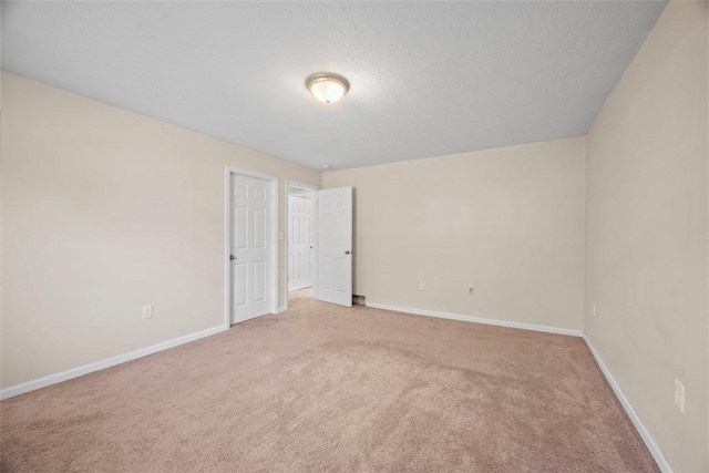 spare room featuring light colored carpet, baseboards, and a textured ceiling