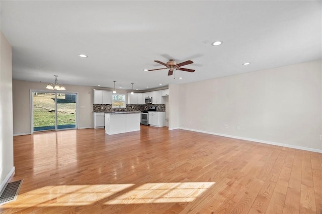 unfurnished living room featuring visible vents, ceiling fan with notable chandelier, recessed lighting, light wood finished floors, and baseboards