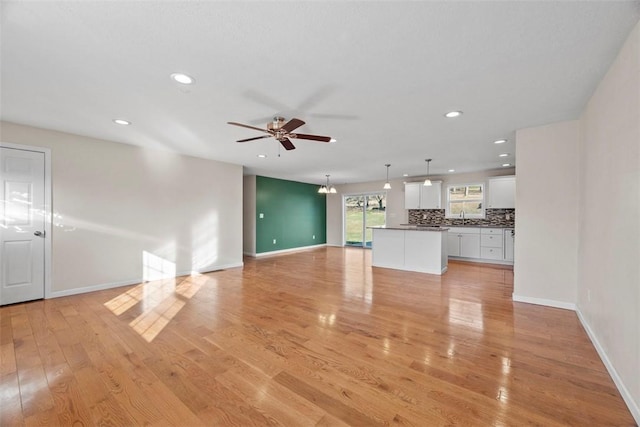 unfurnished living room featuring ceiling fan with notable chandelier, light wood-style floors, baseboards, and a sink