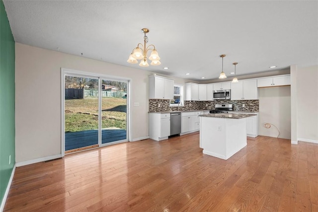 kitchen with dark countertops, white cabinetry, appliances with stainless steel finishes, light wood finished floors, and decorative backsplash