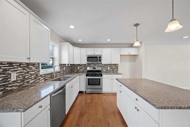 kitchen featuring wood finished floors, a sink, stainless steel appliances, white cabinets, and tasteful backsplash