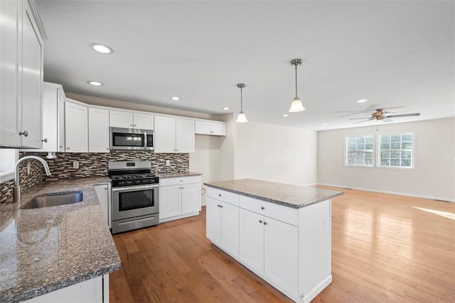 kitchen featuring a sink, white cabinetry, stainless steel appliances, light wood-style floors, and decorative backsplash