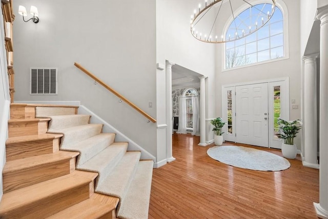 foyer featuring visible vents, stairway, decorative columns, a high ceiling, and wood finished floors