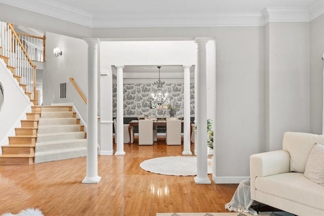 foyer with decorative columns, wood finished floors, ornamental molding, and stairway