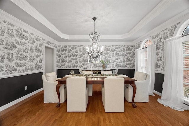 dining area featuring a wainscoted wall, wallpapered walls, a raised ceiling, and wood finished floors