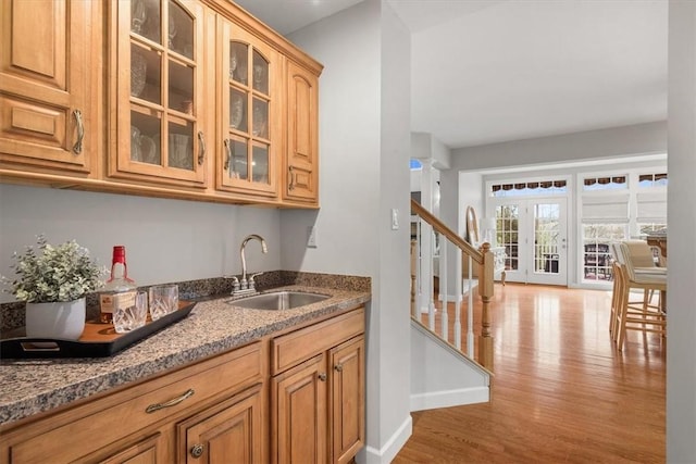 bar featuring a sink, stairway, baseboards, and light wood-style flooring