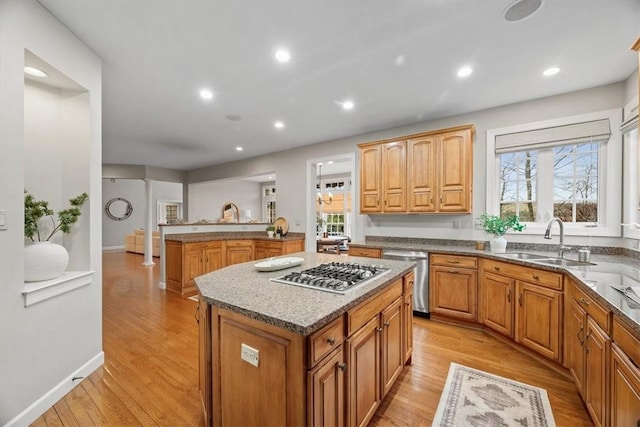 kitchen featuring light wood finished floors, a kitchen island, stone counters, appliances with stainless steel finishes, and a sink