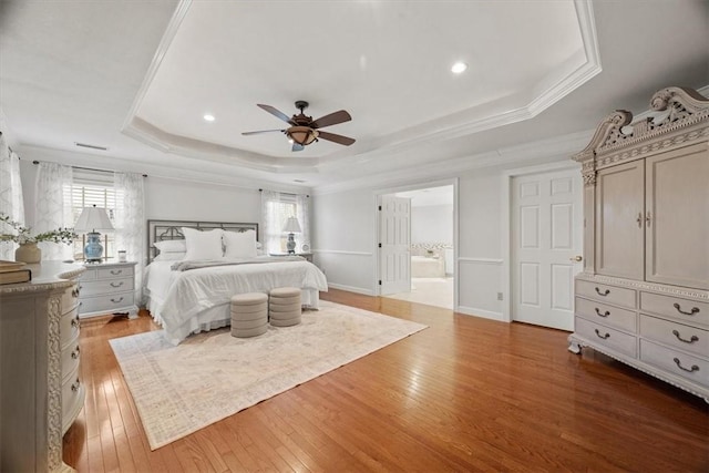 bedroom featuring connected bathroom, baseboards, a tray ceiling, ornamental molding, and light wood-style flooring