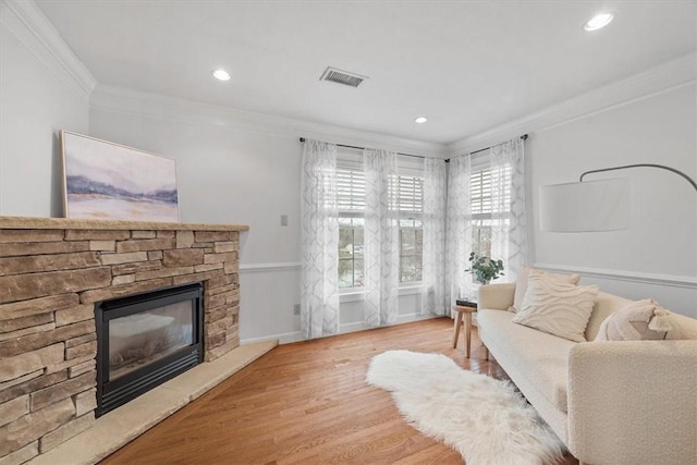 living room with visible vents, ornamental molding, a stone fireplace, recessed lighting, and wood finished floors