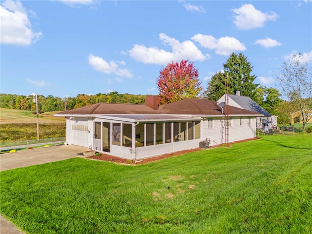 rear view of property featuring concrete driveway, a sunroom, a chimney, a yard, and a garage