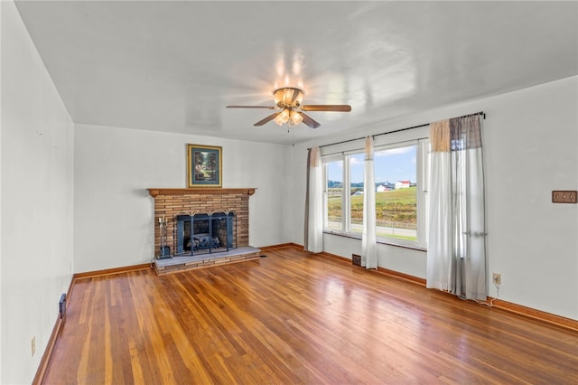 unfurnished living room featuring baseboards, a ceiling fan, wood finished floors, and a fireplace