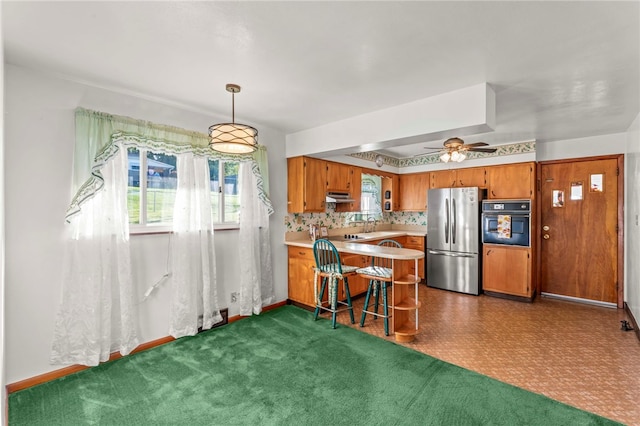 kitchen with oven, brown cabinets, freestanding refrigerator, a peninsula, and light countertops