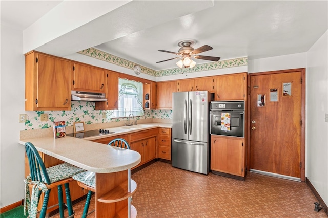 kitchen with under cabinet range hood, light countertops, a peninsula, black appliances, and a sink