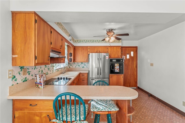 kitchen with black appliances, under cabinet range hood, a sink, light countertops, and baseboards