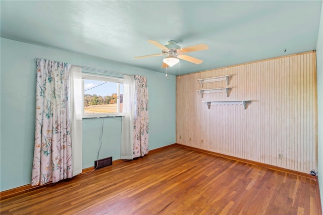 empty room with ceiling fan, visible vents, baseboards, and wood finished floors