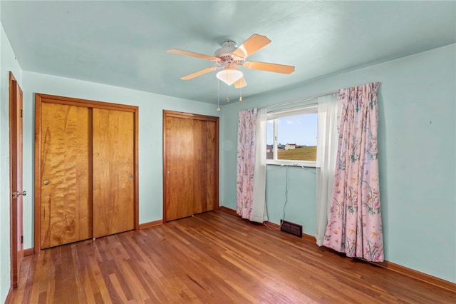 unfurnished bedroom featuring visible vents, baseboards, multiple closets, wood finished floors, and a ceiling fan