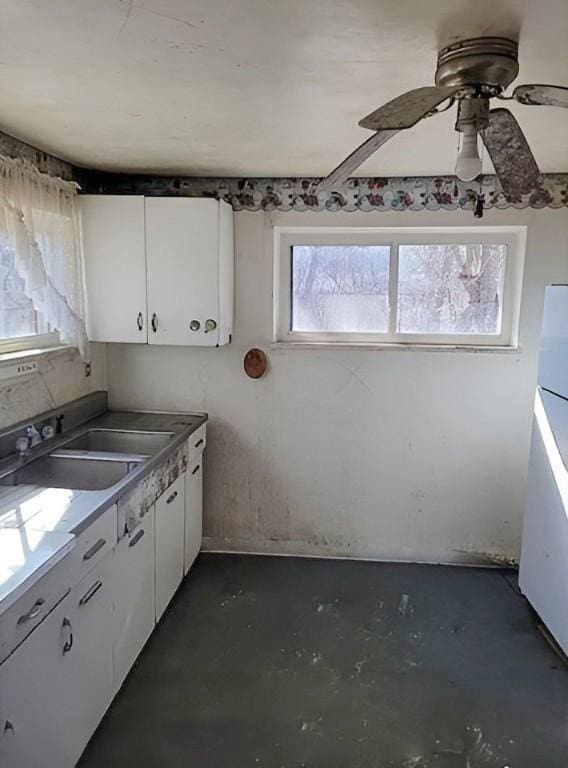 kitchen featuring a sink, concrete floors, white cabinets, and a ceiling fan