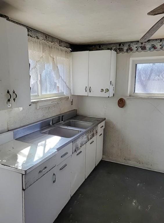 kitchen featuring a sink, concrete flooring, ceiling fan, and white cabinetry