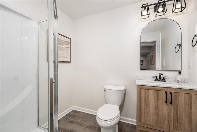 bathroom with a shower stall, baseboards, toilet, wood finished floors, and vanity