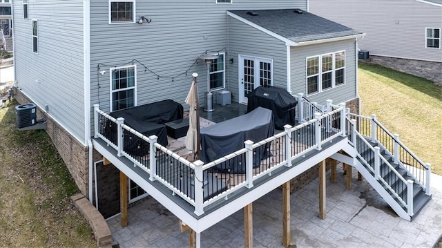 rear view of house featuring a deck, a lawn, a shingled roof, and central AC