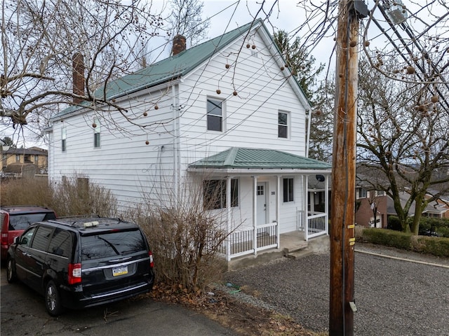 view of front facade with metal roof, covered porch, and a chimney