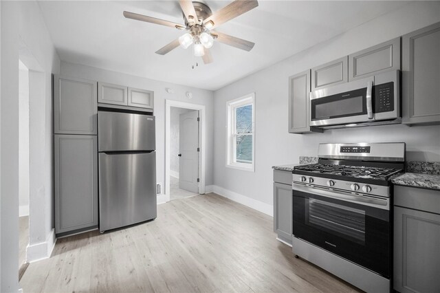 kitchen featuring light stone counters, baseboards, gray cabinets, stainless steel appliances, and light wood-type flooring