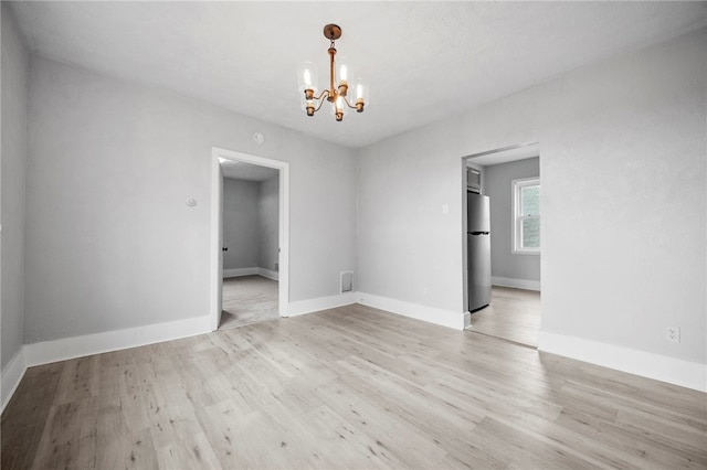 empty room featuring visible vents, baseboards, a notable chandelier, and light wood-style flooring